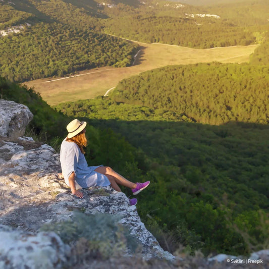 Frau am Felsenrand schaut vom Berg herunter ins Grüne