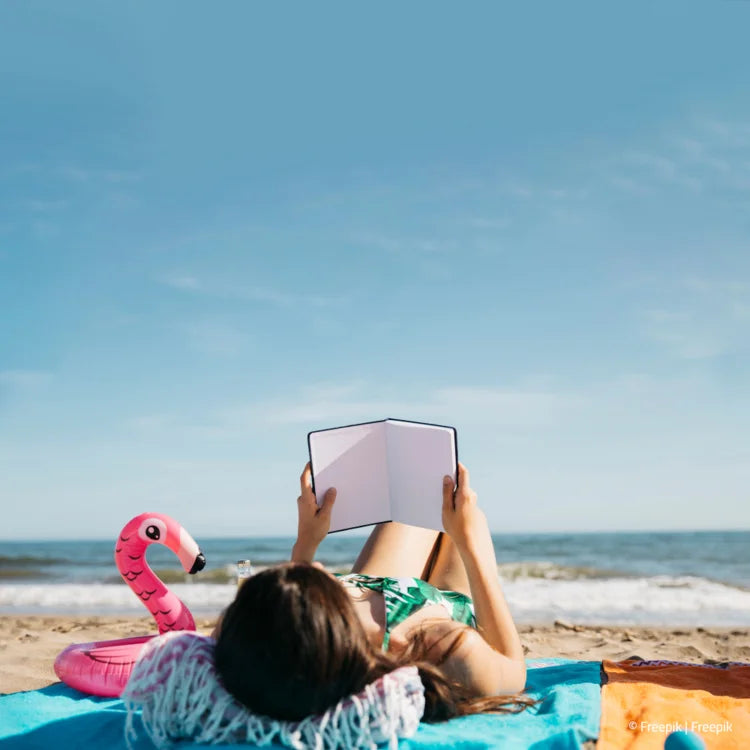 Frau liegt am Strand und liest ein Buch