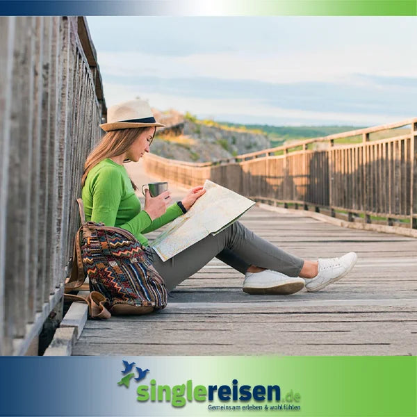 Eine Frau mit Strohhut sitzt mit einer Landkarte und einem Becher auf einer Holzbrücke und plant ihre Reise – Frühbucher-Angebote auf singlereisen.de.