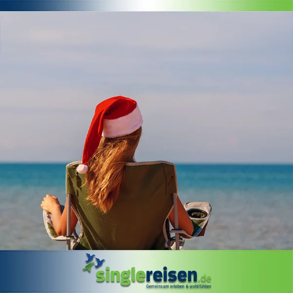Eine Frau mit einer roten Weihnachtsmütze sitzt von hinten zu sehen in einem Campingstuhl am Strand und blickt aufs Meer – Weihnachten & Silvester auf singlereisen.de.